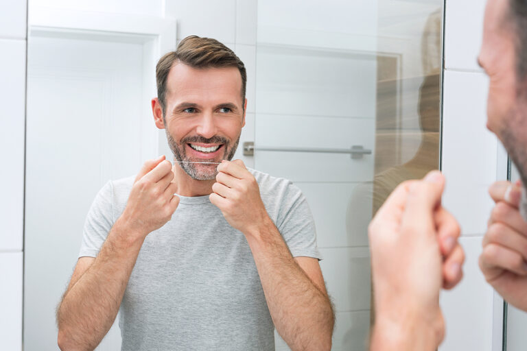 Man Using Dental Floss In The Bathroom. White Teeth And A Beauti